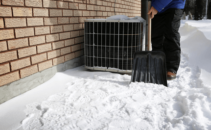 Man shoveling snow around his heat pump.